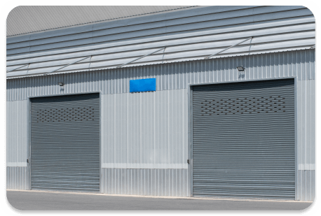 Two large, closed gray roller doors on a building with a corrugated metal wall.